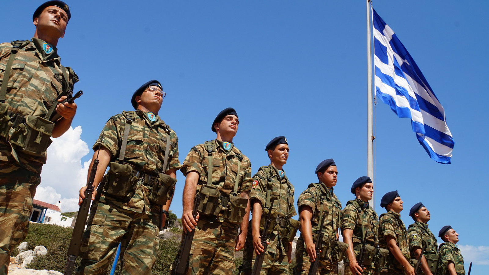 Στρατιώτες, φαντάροι σε στάση προσοχής με φόντο την ελληνική σημαία