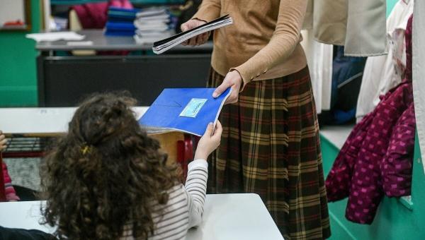 Δασκάλα δίνει τετράδιο σε μικρή μαθήτρια στην τάξη