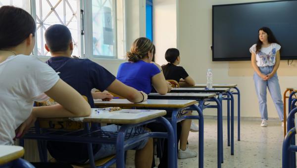 Μαθητές δίνουν πανελλήνιες, κάθονται σε θρανία και τους μιλάει δασκάλα