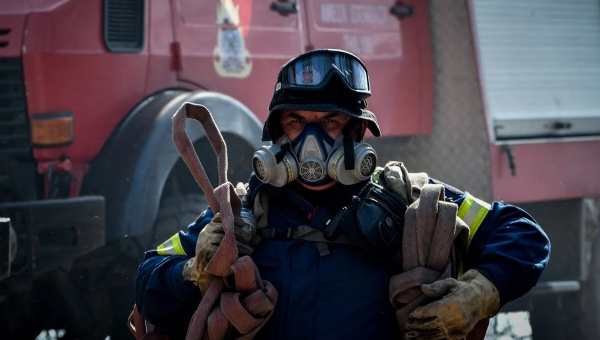 Πυροσβέστης με μάνικα και πίσω του όχημα της Πυροσβεστικής