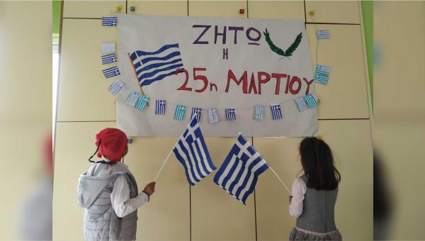 Μαθητές με ελληνική σημαία κοιτάνε πινακίδα που γράφει ζήτω η 25η Μαρτίου
