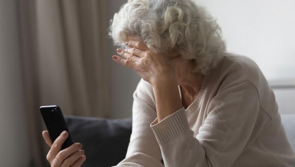 Ηλικιωμένη γυναίκα κοιτάει τηλέφωνο και κρατάει το κεφάλι της