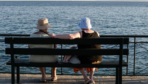 Γυναίκες συνταξιούχοι κάθονται σε παγκάκι και κοιτάνε τη θάλασσα το καλοκαίρι