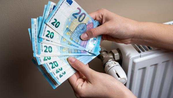 Χέρια μετράνε χρήματα για το επίδομα θέρμανσης δίπλα σε καλοριφέρ