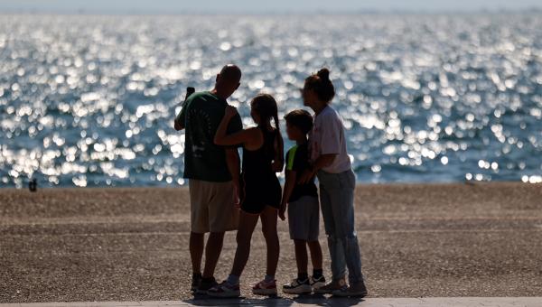 Οικογένεια που θα πάρει το έκτακτο επίδομα παιδιού κοιτάζει τη θάλασσα αγκαλιά