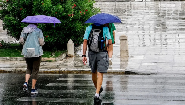 Πολίτες με ομπρέλες σε βρεγμένο δρόμο κατά τη διάρκεια ανοιξιάτικης κακοκαιρίας με βροχές και άστατο καιρό
