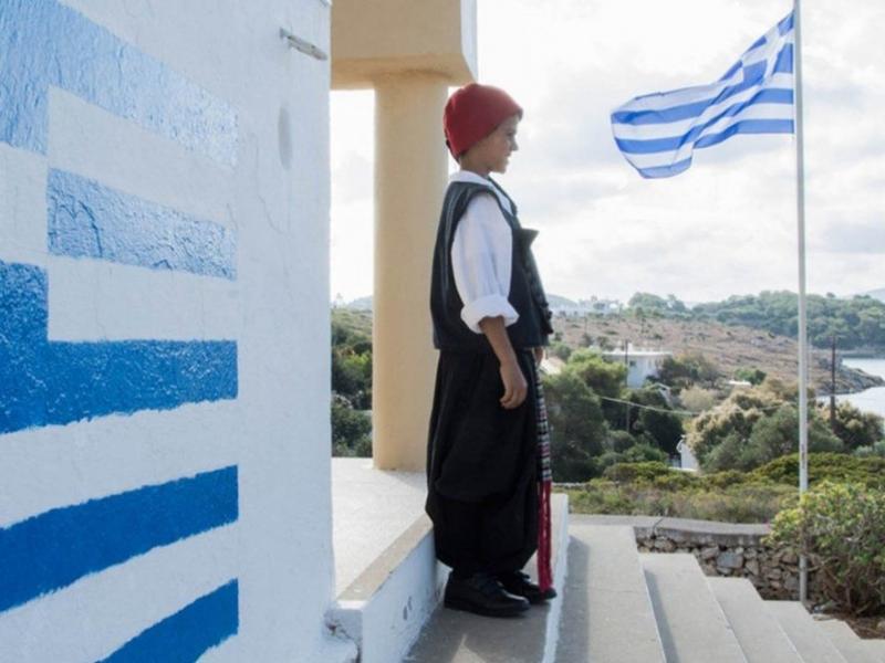 Μαθητής σε σχολείο με παραδοσιακή στολή και την Ελληνική σημαία