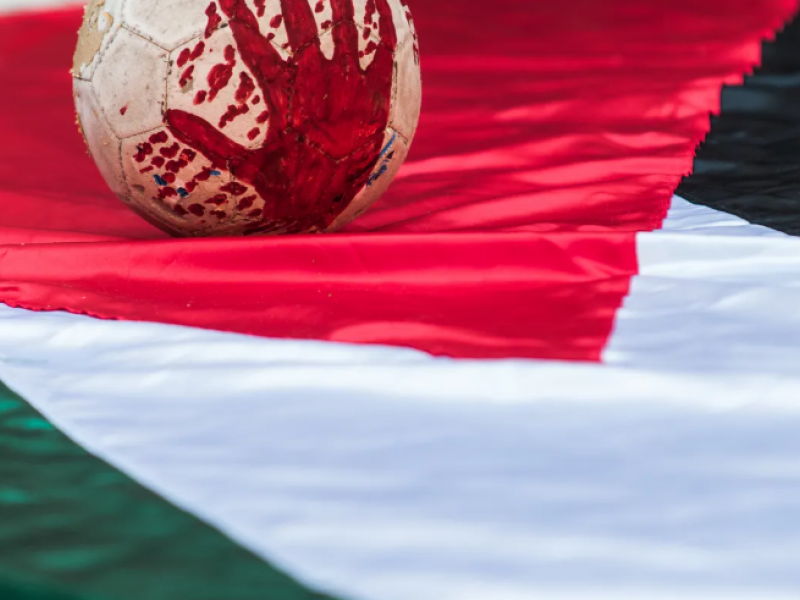 Μπάλα ποδοσφαίρου βαμμένη με αίμα πάνω σε σημαία της Παλαιστίνης