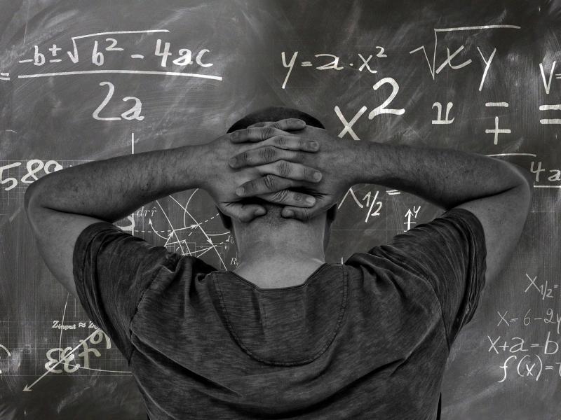 Εκπαιδευτικός με τα χέρια πίσω από το κεφάλι, μπροστά σε πίνακα με μαθηματικά