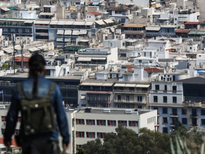 Γυναίκα κοιτάει πανοραμικά τα σπίτια στην Αθήνα από λόφο