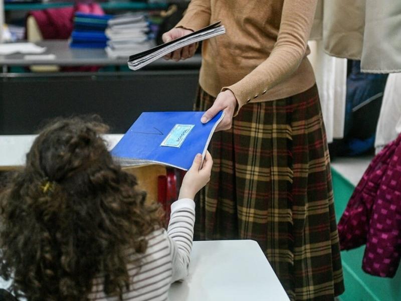 Δασκάλα δίνει τετράδιο σε μικρή μαθήτρια στην τάξη