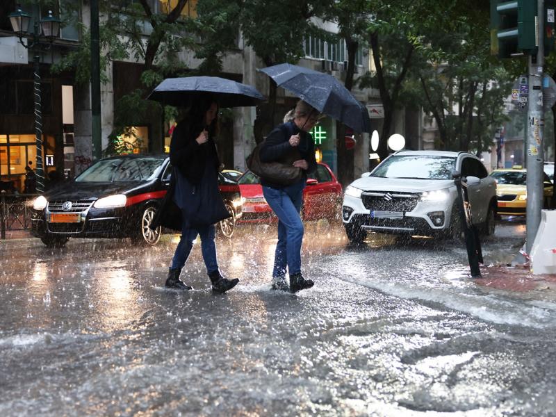 κακοκαιρία, ΕΜΥ, άνθρωποι με ομπρέλες προχωρούν σε πλημμυρισμένο δρόμο