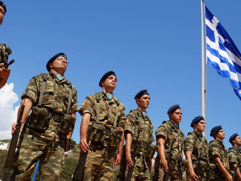 Στρατιώτες, φαντάροι σε στάση προσοχής με φόντο την ελληνική σημαία