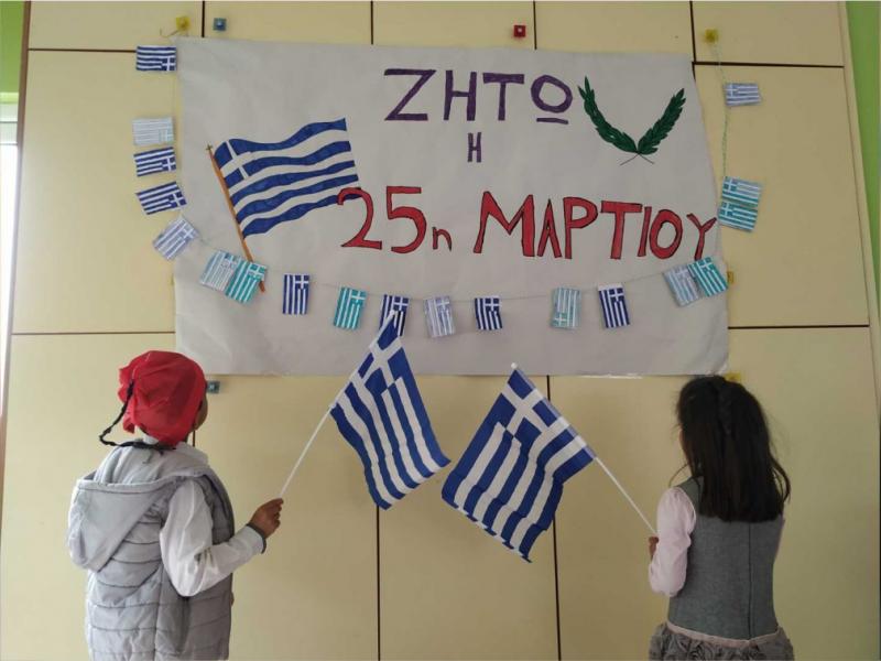 Μαθητές με ελληνική σημαία κοιτάνε πινακίδα που γράφει ζήτω η 25η Μαρτίου