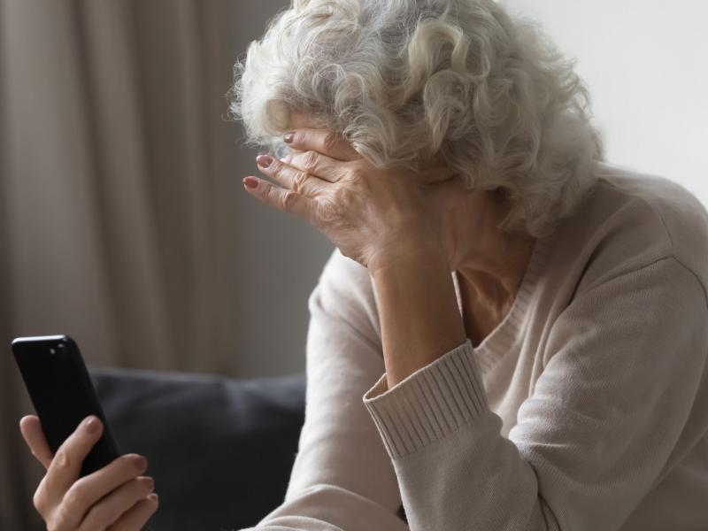 Ηλικιωμένη γυναίκα κοιτάει τηλέφωνο και κρατάει το κεφάλι της