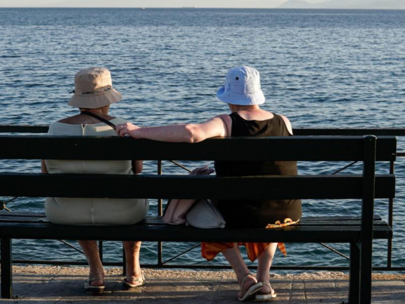 Γυναίκες συνταξιούχοι κάθονται σε παγκάκι και κοιτάνε τη θάλασσα το καλοκαίρι
