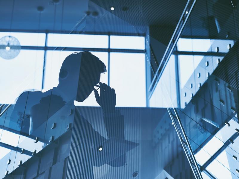 Άνδρας με κοστούμι και γυαλιά σε φόντο τζαμαρίας που φαίνεται μόνο η σκιά του