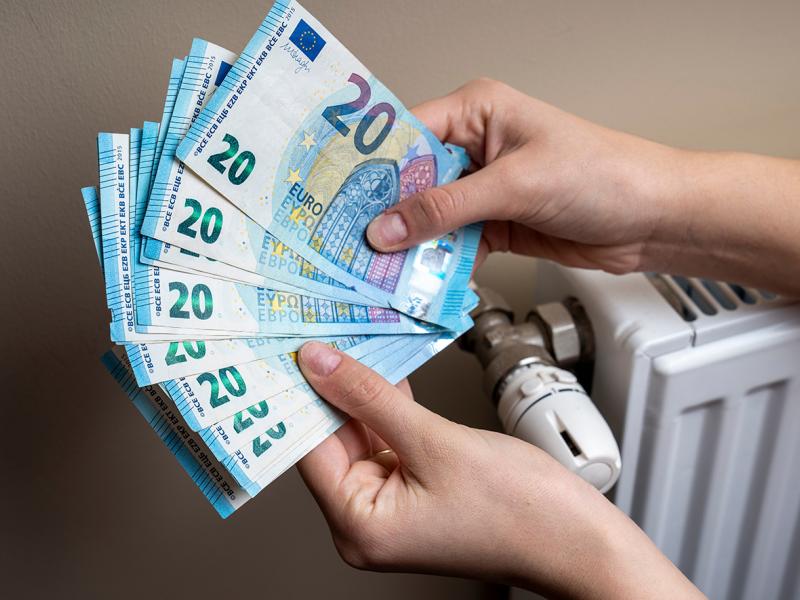 Χέρια μετράνε χρήματα για το επίδομα θέρμανσης δίπλα σε καλοριφέρ