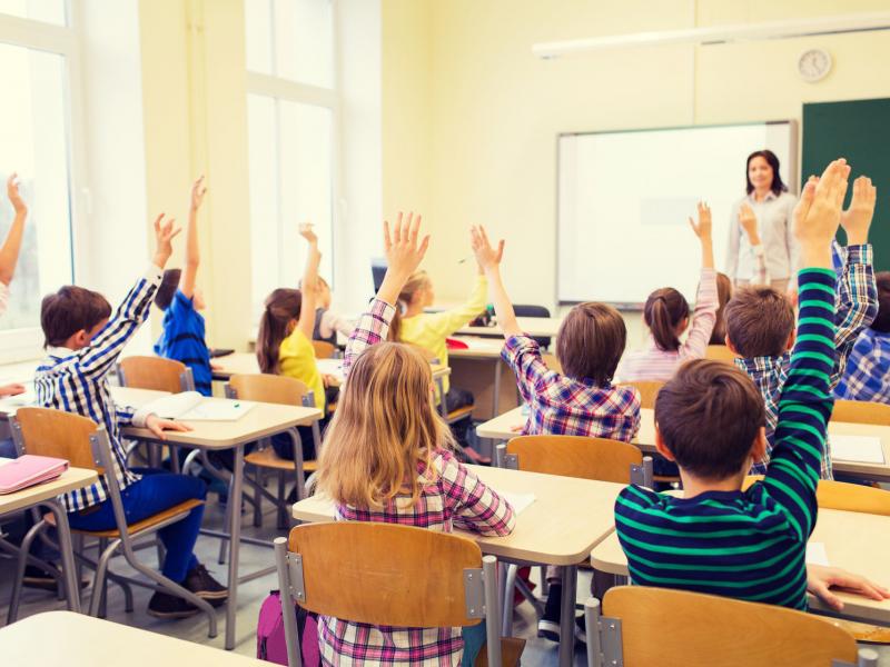 group-of-school-kids-with-teacher-sitting-in-classroom-and-raising-hands_0.jpg