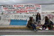 Εκπαιδευτικοί κάθονται σε πεζοδρόμιο με πανό από πίσω τους