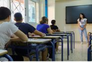 Μαθητές δίνουν πανελλήνιες, κάθονται σε θρανία και τους μιλάει δασκάλα