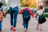 Μητέρα κρατάει τα 3 της παιδιά από το χέρι που πάνε σχολείο φορώντας τσάντες