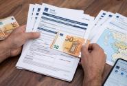 Μια κοντινή φωτογραφία, τραβηγμένη από ψηλά, που δείχνει ένα ζευγάρι τριχωτά ανδρικά χέρια να κρατούν και να χειρίζονται επίσημα έγγραφα πάνω σε ένα ξύλινο γραφείο. Το αριστερό χέρι κρατά μια στοίβα εγγράφων, με την κορυφαία σελίδα να φέρει τον τίτλο «AITHΣH ΕΠΙΣΤΡΟΦΗΣ ΕΝΟΙΚΙΟΥ»