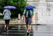 Πολίτες με ομπρέλες σε βρεγμένο δρόμο κατά τη διάρκεια ανοιξιάτικης κακοκαιρίας με βροχές και άστατο καιρό