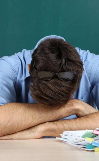 Δάσκαλος κουρασμένος ξαπλώνει πάνω στα χέρια του στην έδρα