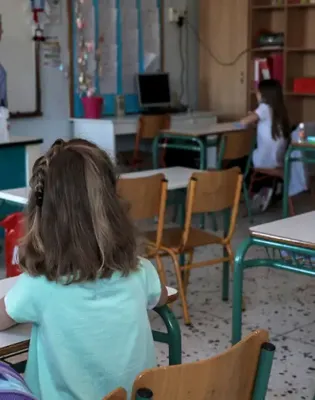 Μαθητές σε θρανία σε σχολείο με δασκάλα στο βάθος