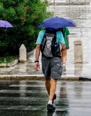 Πολίτες με ομπρέλες σε βρεγμένο δρόμο κατά τη διάρκεια ανοιξιάτικης κακοκαιρίας με βροχές και άστατο καιρό
