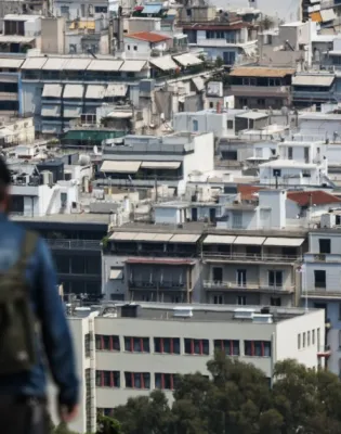 Γυναίκα κοιτάει πανοραμικά τα σπίτια στην Αθήνα από λόφο