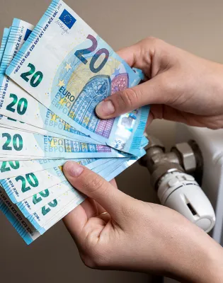 Χέρια μετράνε χρήματα για το επίδομα θέρμανσης δίπλα σε καλοριφέρ