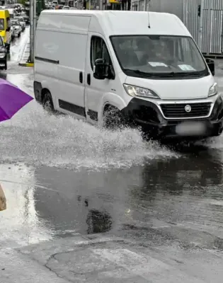 Γυναίκα περπατάει με ομπρέλα εν μέσω κακοκαιρίας ενώ αμάξια είναι σε βρεγμένο δρόμο