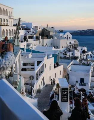 Γυναίκα τραβάει φωτογραφία τη Σαντορίνη κατά το ηλιοβασίλεμα, για το πρόγραμμα Τουρισμός για Όλους 2026-2027.