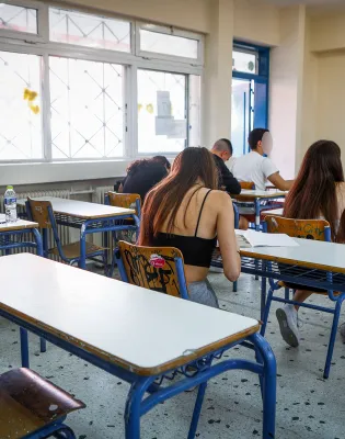 Μαθητές δίνουν εξετάσεις σε τάξη με εκπαιδευτικό να τους επιβλέπει
