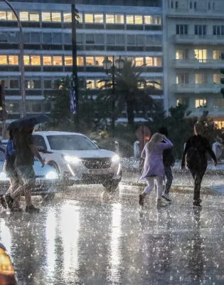 Κόσμος με ομπρέλες σε κακό καιρό στο Σύνταγμα περνάει το δρόμο ενώ έχει καταιγίδα