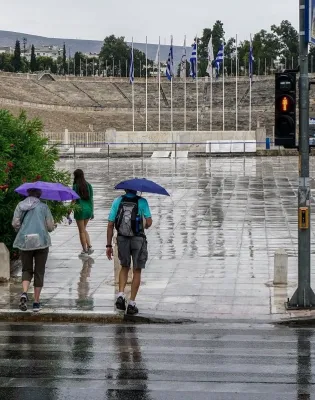 Άνθρωποι με ομπρέλες στο Καλλιμάρμαρο ενώ βρέχει στην Αττική