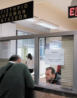 Εσωτερικό δημόσιας υπηρεσίας με πολίτη σε γκισέ που φέρει την επιγραφή «Λογιστήριο Πληρωμών Συντάξεων» και ψηφιακό πίνακα προτεραιότητας