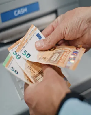Ηλικιωμένος συνταξιούχος μετράει τη σύνταξή του σε χρήματα μπροστά από τράπεζα