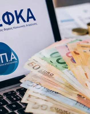 Λογότυπο ΕΦΚΑ και ΔΥΠΑ σε υπολογιστή και στο πληκτρολόγιο φαίνονται χρήματα