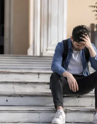 Πτυχιούχος με σκυμμένο κεφάλι μπροστά από Πανεπιστήμιο