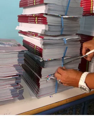 Εκπαιδευτικός κόβει με ψαλίδι ταινία που κρατάει σχολικά βιβλία για να τα μοιράσει σε μαθητές
