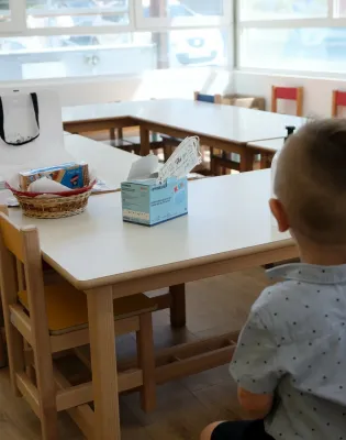 Παιδί νηπιαγωγείου κάθεται σε θρανίο με πλάτη στην κάμερα