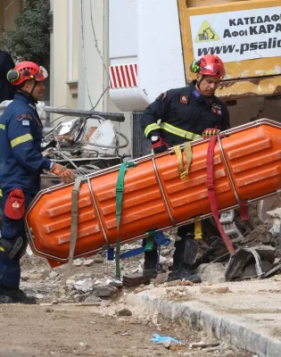 Άνδρες της ΕΜΑΚ μεταφέρουν φορείο για τους νεκρούς στο κτήριο της Πλάκας που έγινε έκρηξη
