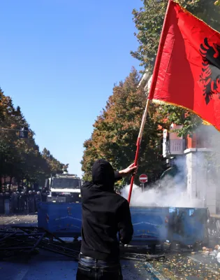 A protester waves an Albanian flag during clashes in Tirana, Albania, Wednesday, Oct. 14, 2026, joining a demonstration organized by the Flamingo protest movement demanding the resignation of Prime Minister Edi Rama. (AP Photo/Hameraldi Agolli)