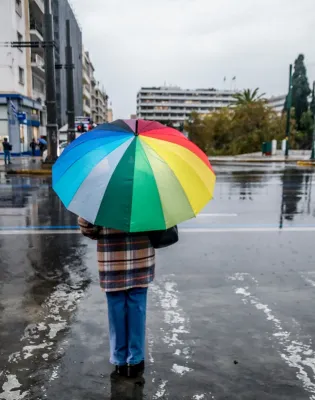 Άτομο κρατά πολύχρωμη ομπρέλα ενώ βρέχει στο Σύνταγμα μπροστά από τη Βουλή