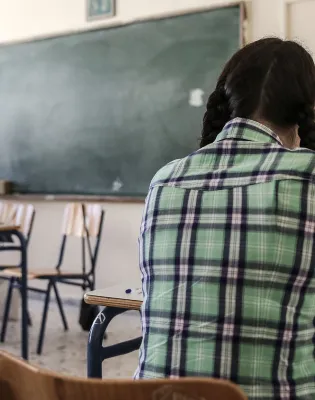 Μαθήτρια με πλάτη στην κάμερα κοιτάζει δασκάλα την ώρα που κάνει μάθημα στην έδρα της τάξης