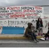 Εκπαιδευτικοί κάθονται σε πεζοδρόμιο με πανό από πίσω τους