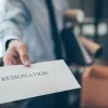 Χέρι ανθρώπου με κοστούμι δίνει φάκελο προς την κάμερα με την αναγραφή resignation